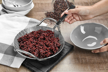 Woman pouring cooked rice from dish into plate on table