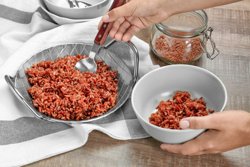 Woman pouring cooked rice from dish into bowl on kitchen table