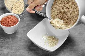 Woman pouring cooked rice from saucepan to plate on table