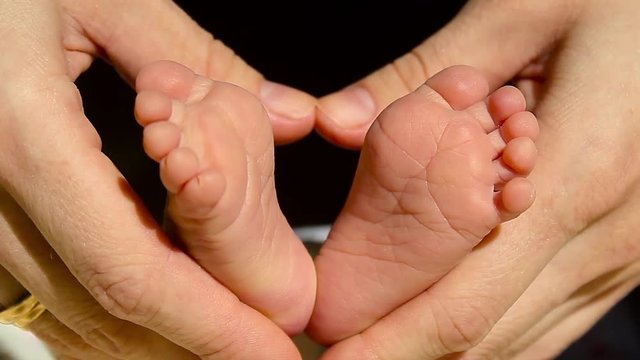Baby feet in mother hands. Tiny Newborn Baby's feet on female Heart Shaped hands closeup. Mom and her Child. Happy Family concept. Beautiful conceptual video of Maternity.
