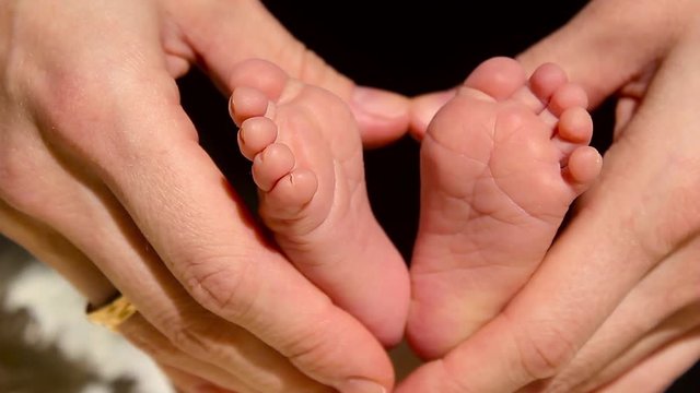 Baby feet in mother hands. Tiny Newborn Baby's feet on female Heart Shaped hands closeup. Mom and her Child. Happy Family concept. Beautiful conceptual video of Maternity.