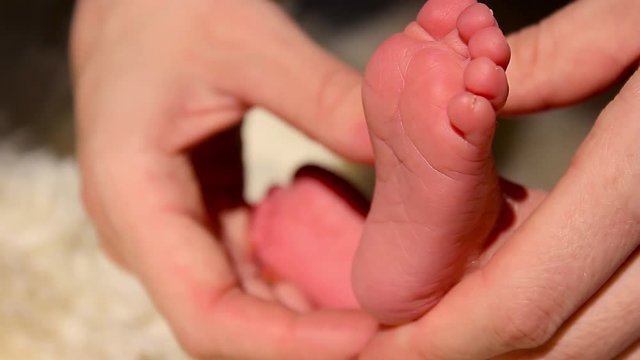 Baby feet in mother hands. Tiny Newborn Baby's feet on female Heart Shaped hands closeup. Mom and her Child. Happy Family concept. Beautiful conceptual video of Maternity.