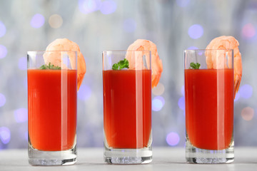 Glasses of tomato sauce and shrimps on table against sparkly background, closeup