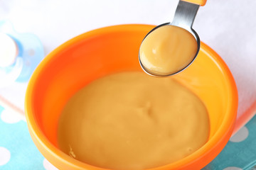 Spoon and bowl with baby food on fabric