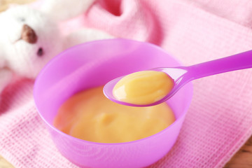 Fototapeta na wymiar Plastic spoon and bowl with baby food on fabric