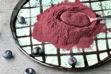Acai powder, berries and metal spoon on plate