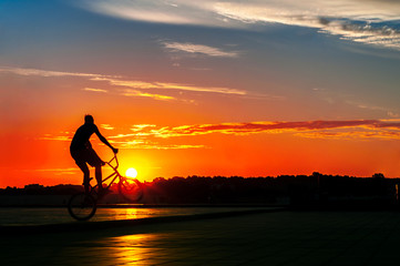 A guy shows tricks on a bicycle at sunset