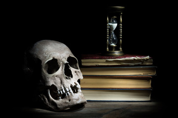 Life is short concept. Skull and vintage hourglass on old books and wooden table