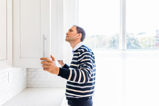 Young man checking looking inside empty kitchen modern cabinets by window after or before moving in