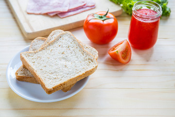 slices of bread with jam and ham, tamoto, lettuce,  on table with kitchen on table with kitchen