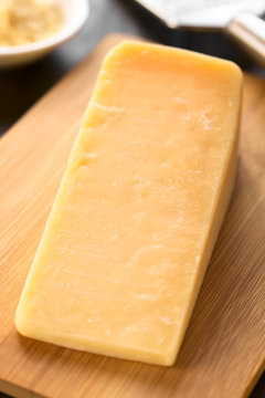 Piece of parmesan-like hard cheese on wooden board with grater in the back, photographed with natural light (Selective Focus, Focus in the middle of the image)