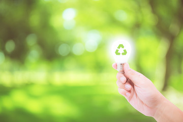 Man hand holding glowing light bulb with recycle symbol on nature background - save energy concept...