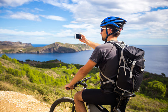 a young guy on a mountain bike trails in Spain and takes a photo on a white phone in the background of the Mediterranean sea of the rocky coast of the Costa Brava. k.
