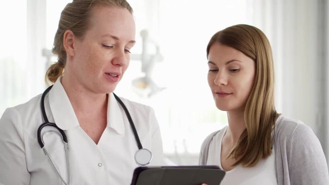 Female professional doctor at work. Woman physician with stethoscope consulting patient in modern clinic. Showing something on tablet
