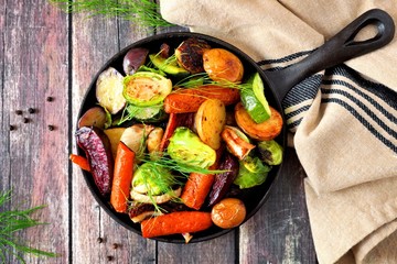 Cast iron skillet of roasted autumn vegetables, overhead scene on a rustic wood background