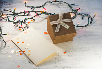 Christmas garland with lights and a gift box with a blank postcard on a light background. Christmas gift.