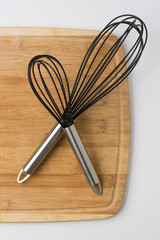 Two Whisks Crossed on Wooden Cutting Board