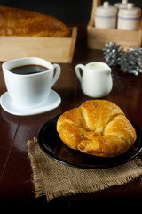 Bread on black plate and black coffee with milk on wooden table