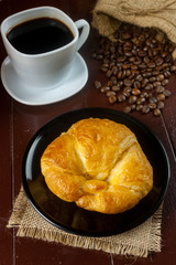 Bread on black plate and black coffee with coffee beans in cloth bag on wooden table