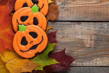 Homemade gingerbread cookies in the shape of pumpkins for Halloween. Autumn maple leaves on old...