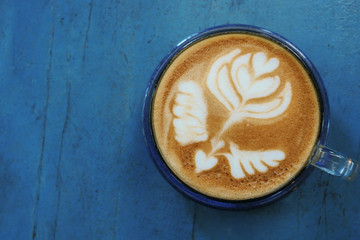 Top view of hot coffee latte cappuccino cup with beautiful latte art milk foam on blue painted wood table background.