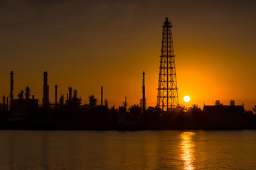 Obraz premium Silhouette oil refinery and petrochemical plant at sunrise time beside Chao Phaya river, Thailand. Light reflection on the smooth water.