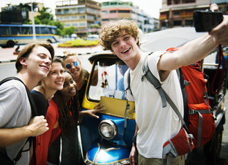 A group of Caucasian tourists taking selfie in front of a Tuk Tuk