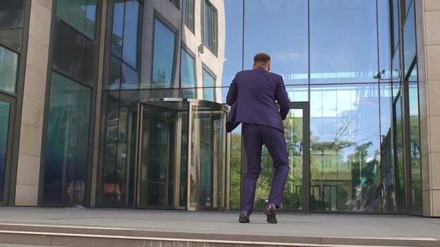 Successful happy businessman stands with his back to the camera and dances near a modern office building.