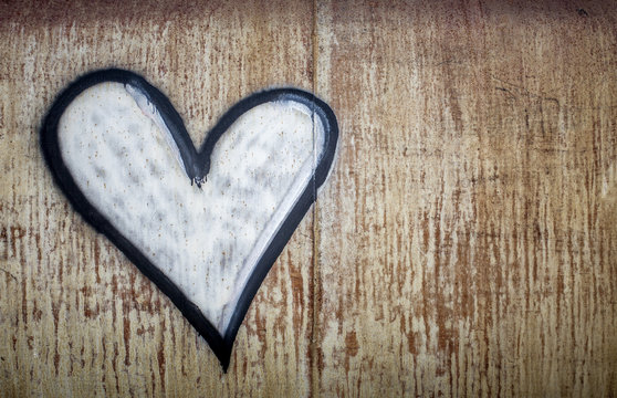 A white spray painted heart outlined in black painted onto a rusted metal backdrop