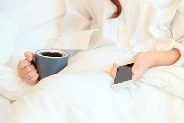 Fototapeta na wymiar young woman drinking coffee in her bedroom and checking her smaitphone in the morning