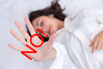 The words NO!. Portrait of a young attractive woman showing stop sign with hand on her bedroom