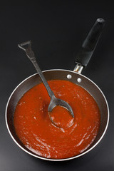Tomato sauce is prepared to cook as a spaghetti or pasta in Italian style in a black pan on a black background.top view