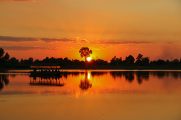 Silhouette photo of people exploring on the boat in the evening with Sunset over the lake and the  reflection.Orange sky background.