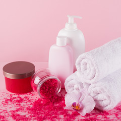 Obraz na płótnie Canvas Towels with shower gel, scrub, sea salt and body lotion on pink background.
