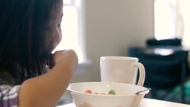 Little asian girl hops up before she eats her cereal and gives a thumbs up