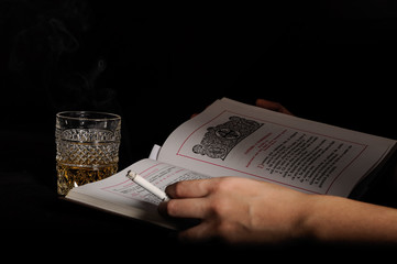 Naklejka premium Woman hands smoking and drinking - Close up of adult woman hands holding a cigarette near a glass of alcohol and reading a Bible