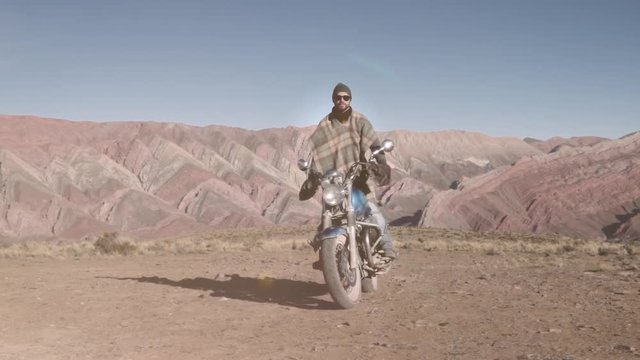 Man riding custom motorcycle in the salt flats of Salar grande in Argentina. Slow motion	Man riding motorcycle on the mountains