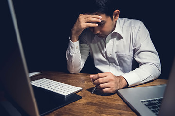 Stressed tired young man feeling headache while working overtime  at night