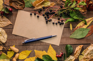 Frame of bright autumn leaves on the boards with a blank page and red apple and blue pen