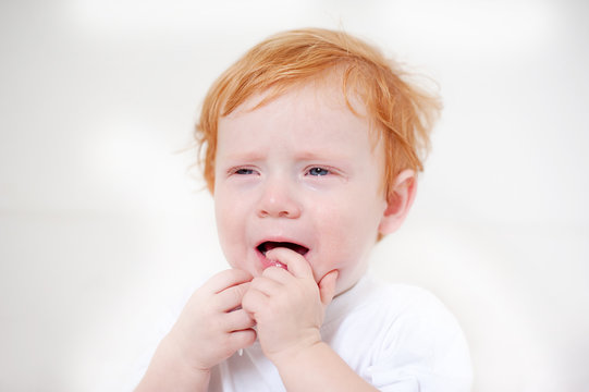 Miserable redhead boy crying on the white background