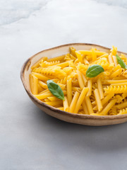 Italian raw short pasta in a dish with basil leaves on gray background