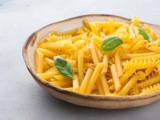 Italian raw short pasta in a dish with basil leaves on gray background