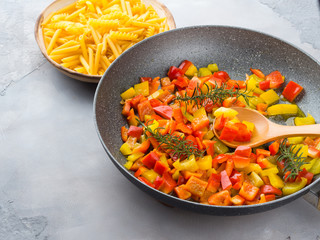 Cooking bell peppers with rosemary in skillet as sauce for italian pasta