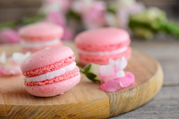 French cakes macaroons. Light pink round macaroons and flowers on a wooden board. Vintage wooden background. Sweets photo. Closeup