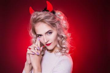 Portrait of a beautiful blonde woman with a cunning look and horns on her head. The dress for the Halloween party. To think something is not good. Evil demon girl is the devil.