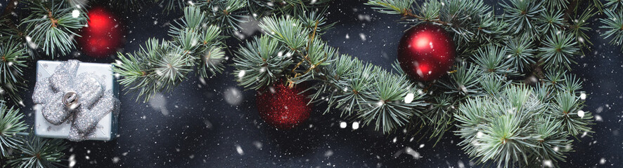 Blue spruce branches with christmas baubles on dark black concrete effect background. Snow fall flakes