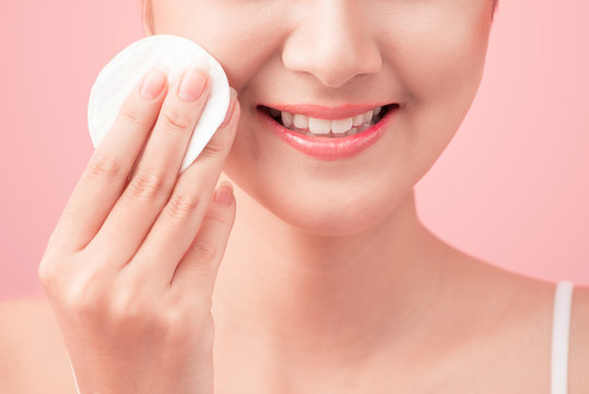 Gorgeous young woman holding cotton pad and smiling in taking care of her face for fresh healthy skincare on pink background
