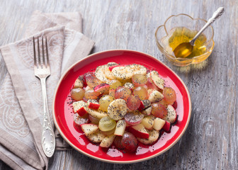 Fruit salad of grapes, bananas and apples with poppy seeds and honey on a wooden table, selective focus. Healthy vegan dessert