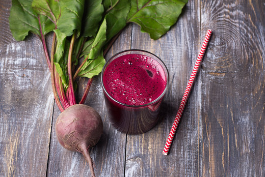 Fresh beet juice in glass with a straw on a wooden background, selective focus. Healthy detox diet