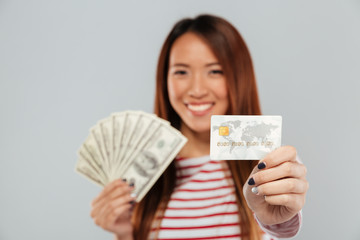 Asian lady over grey wall holding money and credit card.